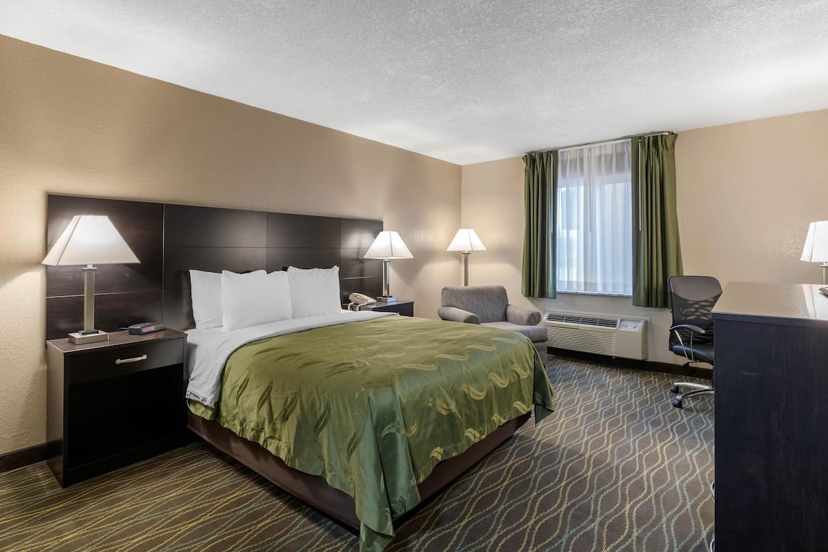 A hotel room with a large bed, two bedside tables with lamps, a desk, and a chair.