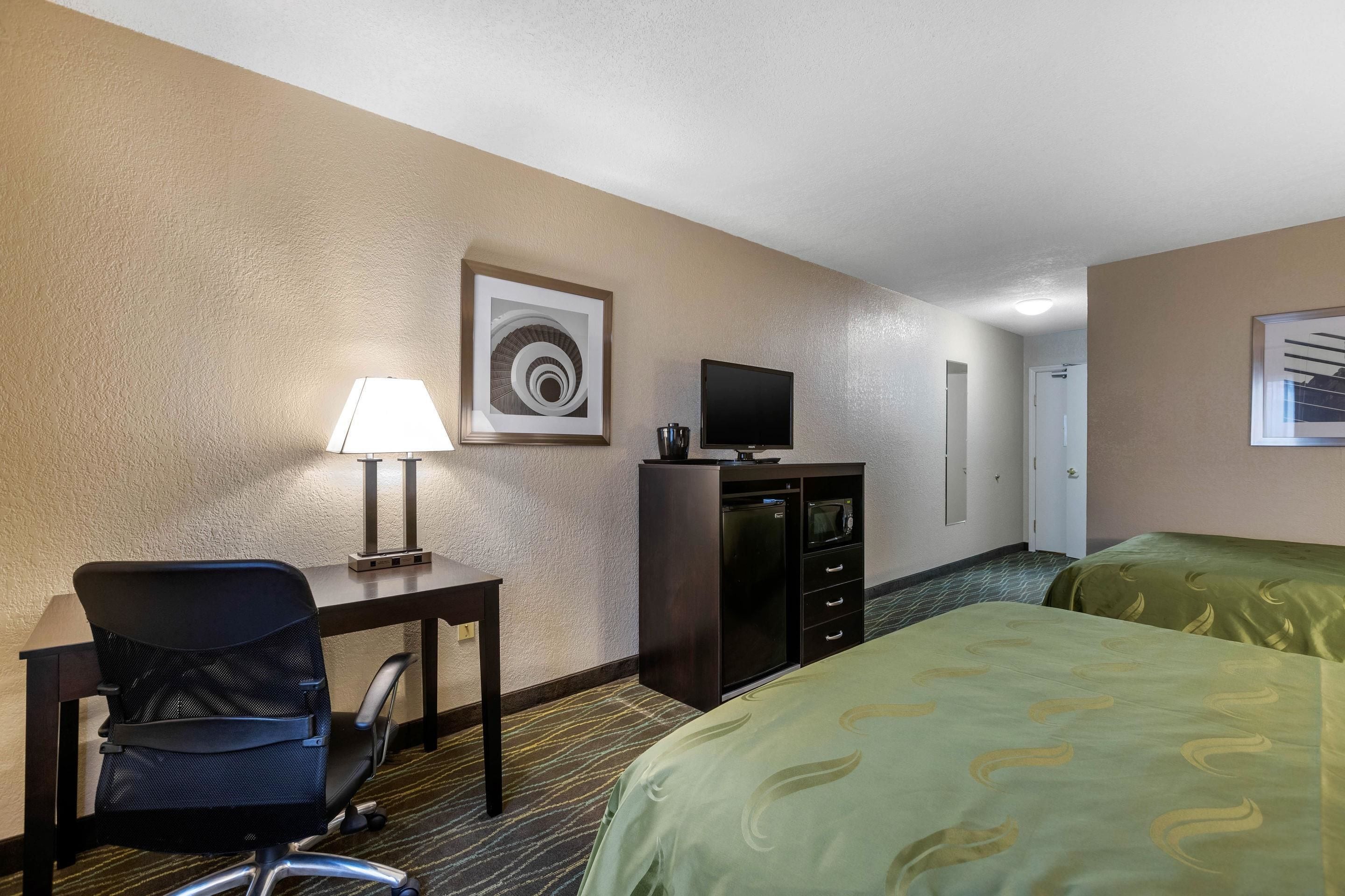 A hotel room with a desk, chair, television, and two beds.