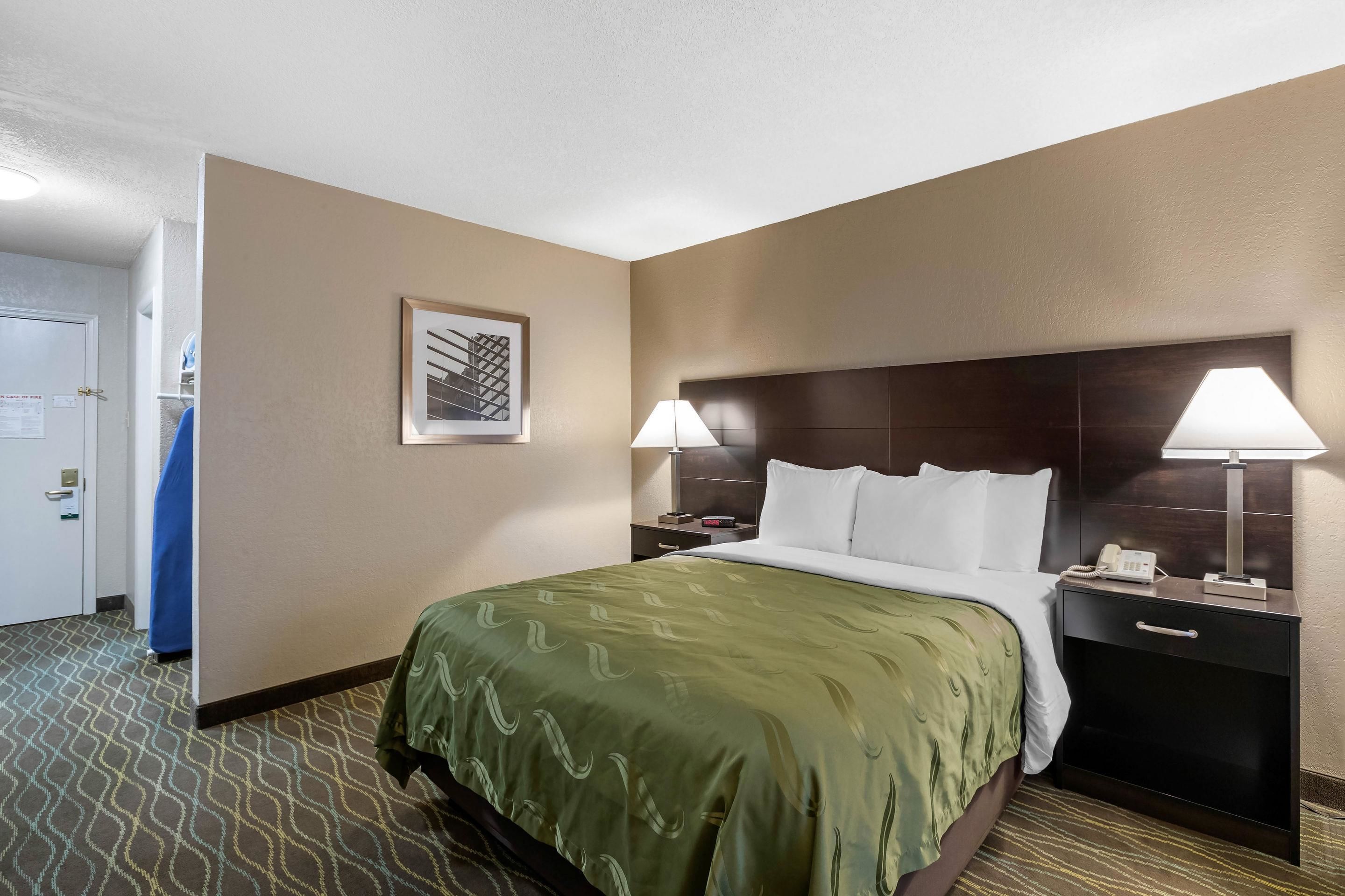 Habitación de hotel con una cama grande, dos lámparas de noche, una mesita con un teléfono y un cuadro enmarcado en la pared.