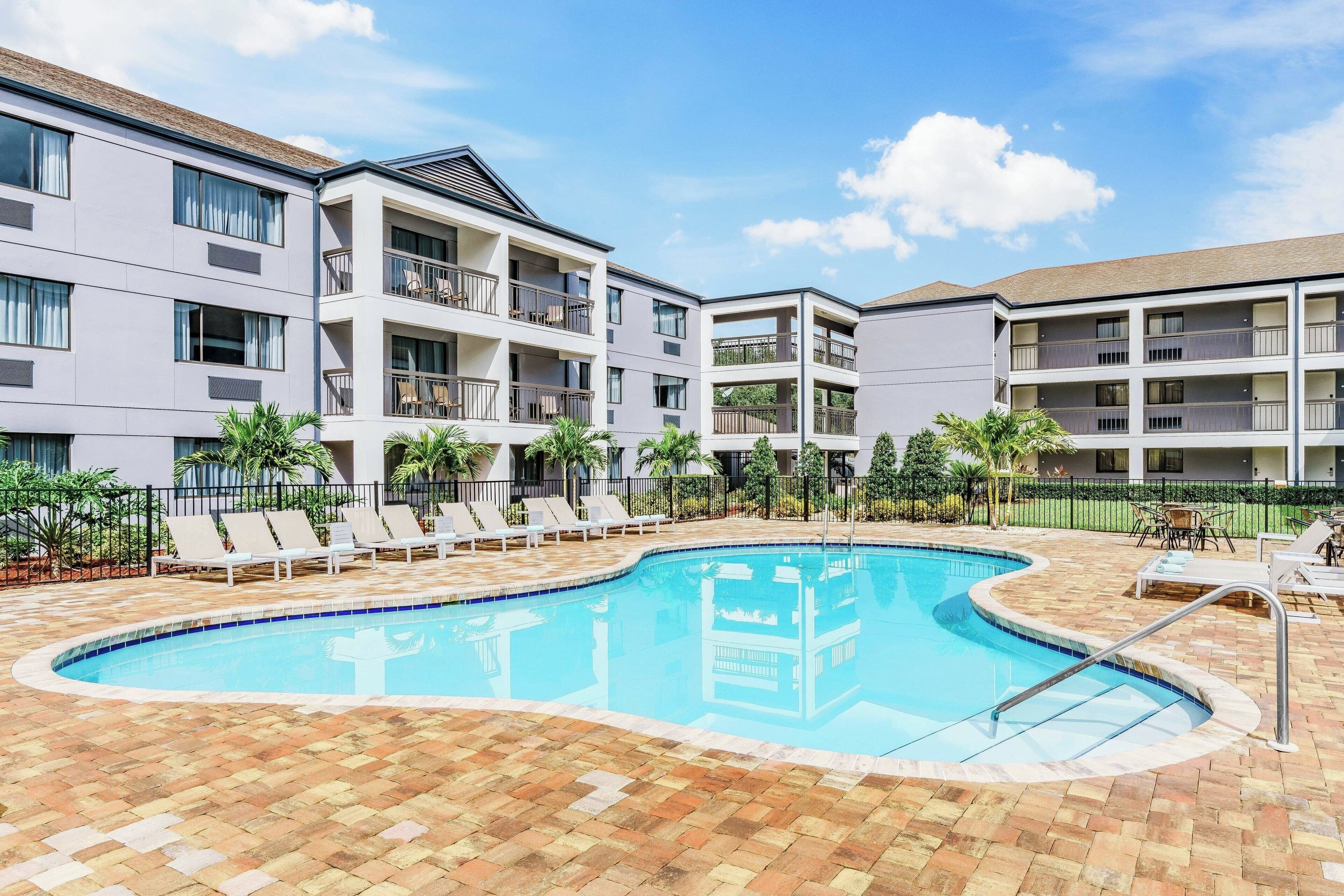Une piscine avec des chaises longues et un immeuble à plusieurs étages doté de balcons.
