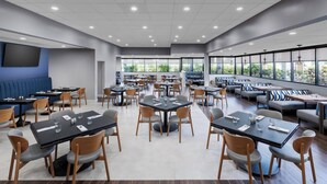 Un comedor amplio con varias mesas y sillas, ventanas grandes que ofrecen luz natural y un diseño moderno con una variedad de opciones de asientos.