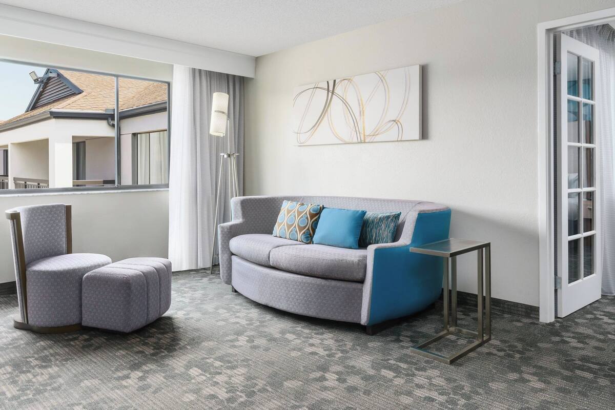 Un soggiorno moderno con un divano grigio, una poltrona abbinata e un piccolo tavolino. Un'ampia finestra offre vista su un edificio con tetto spiovente.