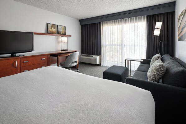 Habitación de hotel con una cama grande, un escritorio con televisor de pantalla plana, una silla, un sofá y una ventana con cortinas.