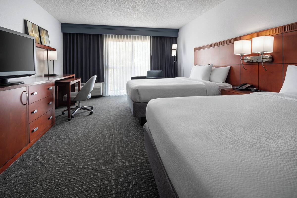 A hotel room with two beds, a desk with a TV, a chair, and a desk lamp.
