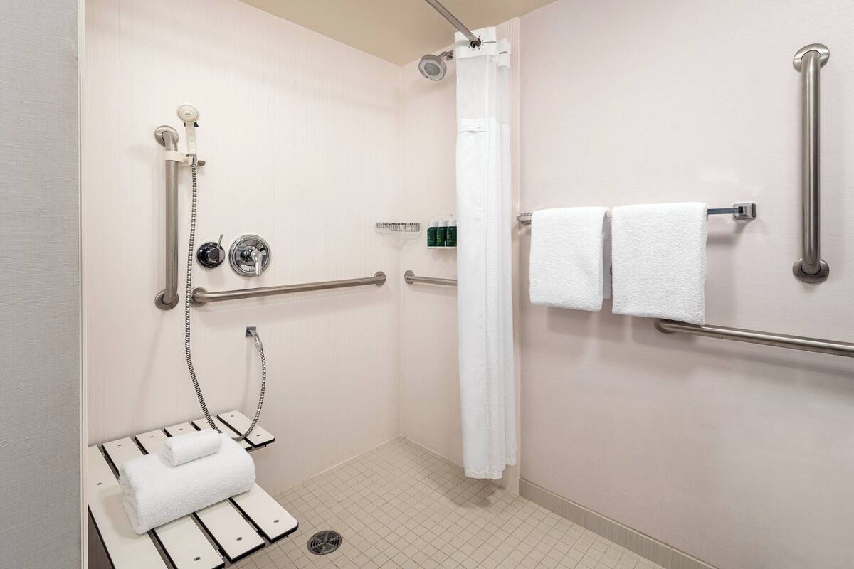 A handicap-accessible bathroom with a shower, grab bars, a towel rack, and a toilet with a white towel.