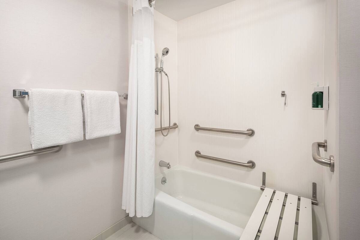 A bathroom with a white bathtub, a shower with a handheld showerhead, and grab bars.