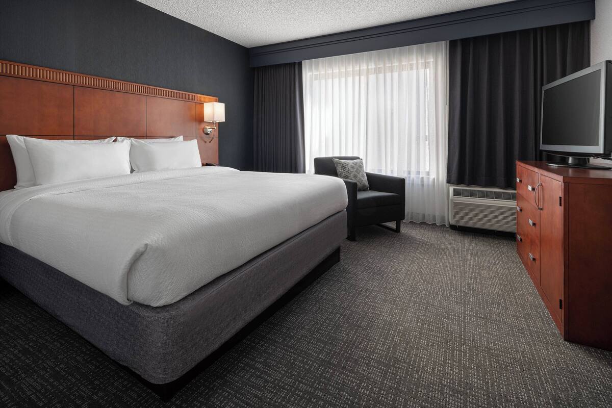 A hotel room with a large bed, a chair, a TV, and a dresser.