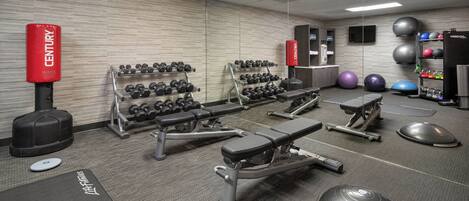A gym with weightlifting equipment, dumbbells, exercise balls, and a bench.
