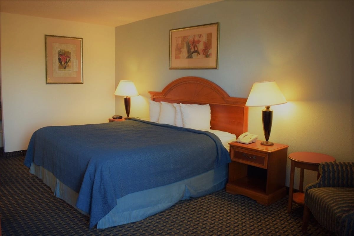 Ett hotellrum med en stor säng, två sängbord med lampor, en stol och två inramade tavlor på väggen.