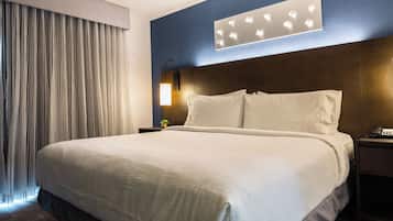 Habitación de hotel con una cama grande, una mesita de noche con lámpara y un aplique de pared.