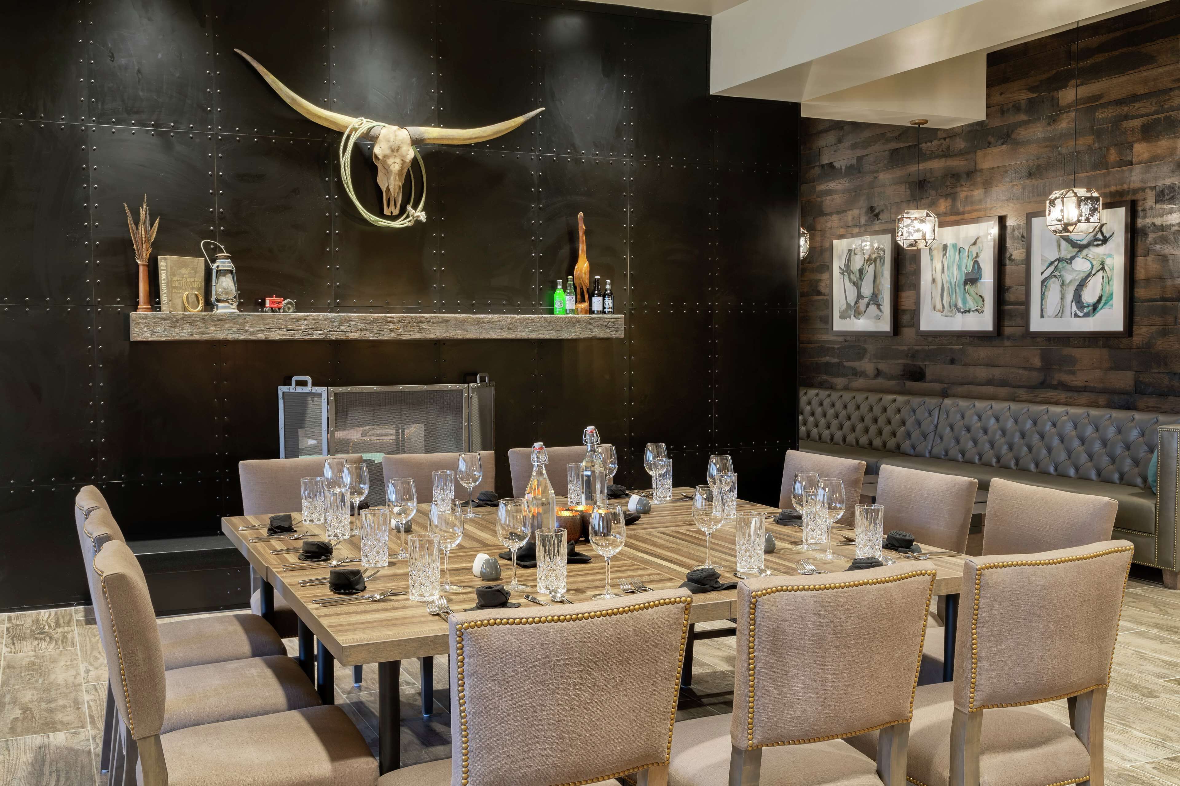 Un comedor con una mesa de madera dispuesta para seis personas, rodeada de sillas tapizadas con detalles dorados. Sobre la mesa, en la pared, cuelga un cráneo de toro grande.