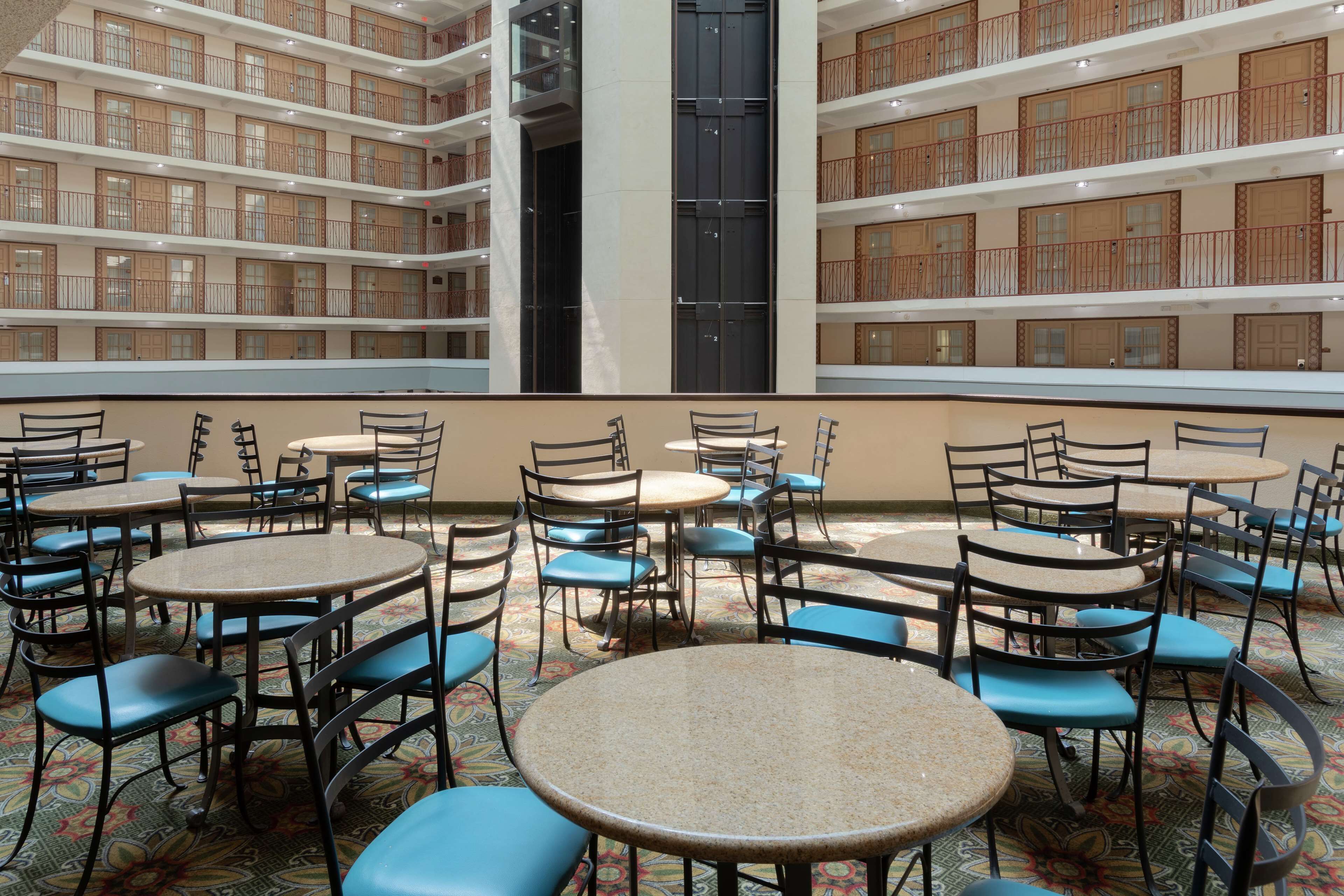 A multi-level atrium with round tables and chairs, featuring a patterned carpet and wooden balconies.