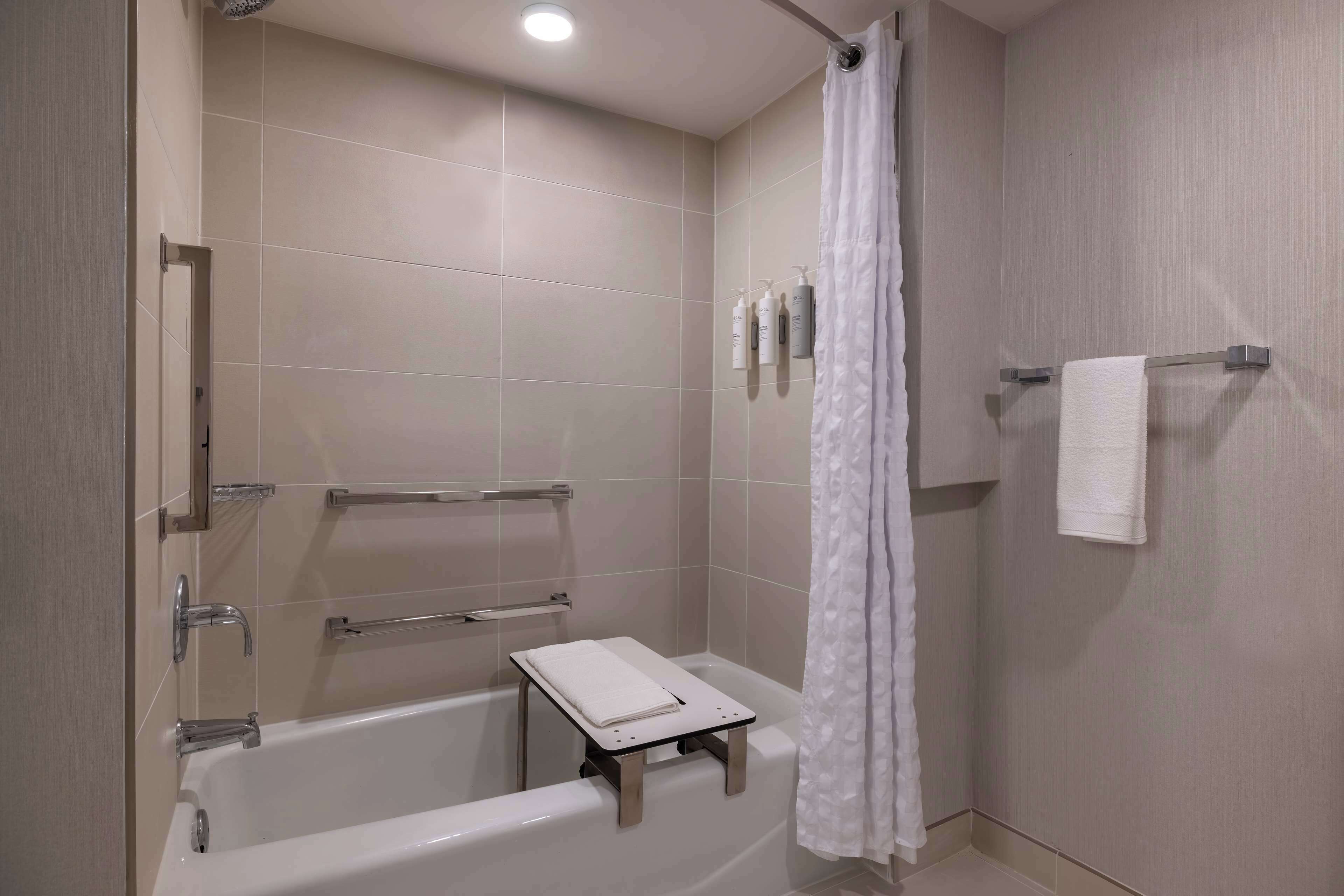 A modern bathroom with a bathtub, a shower curtain, a towel rack, and a small table with a towel.