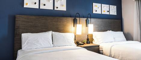 A hotel room with two beds, a wooden headboard, bedside tables with lamps, and wall art.