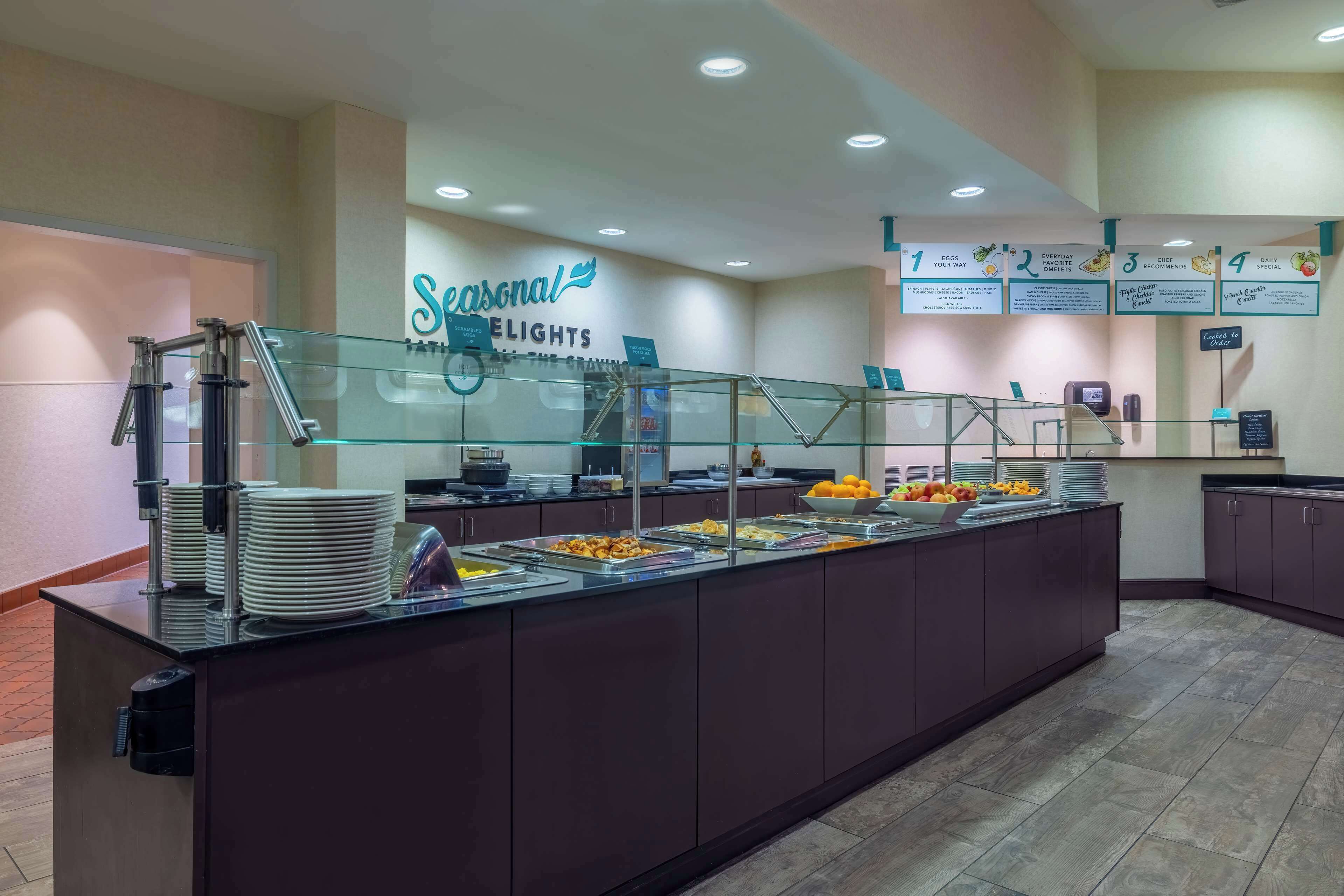 A buffet area with a glass partition, a sign reading "Seasonal ELIGHTS", and a menu board with breakfast options.