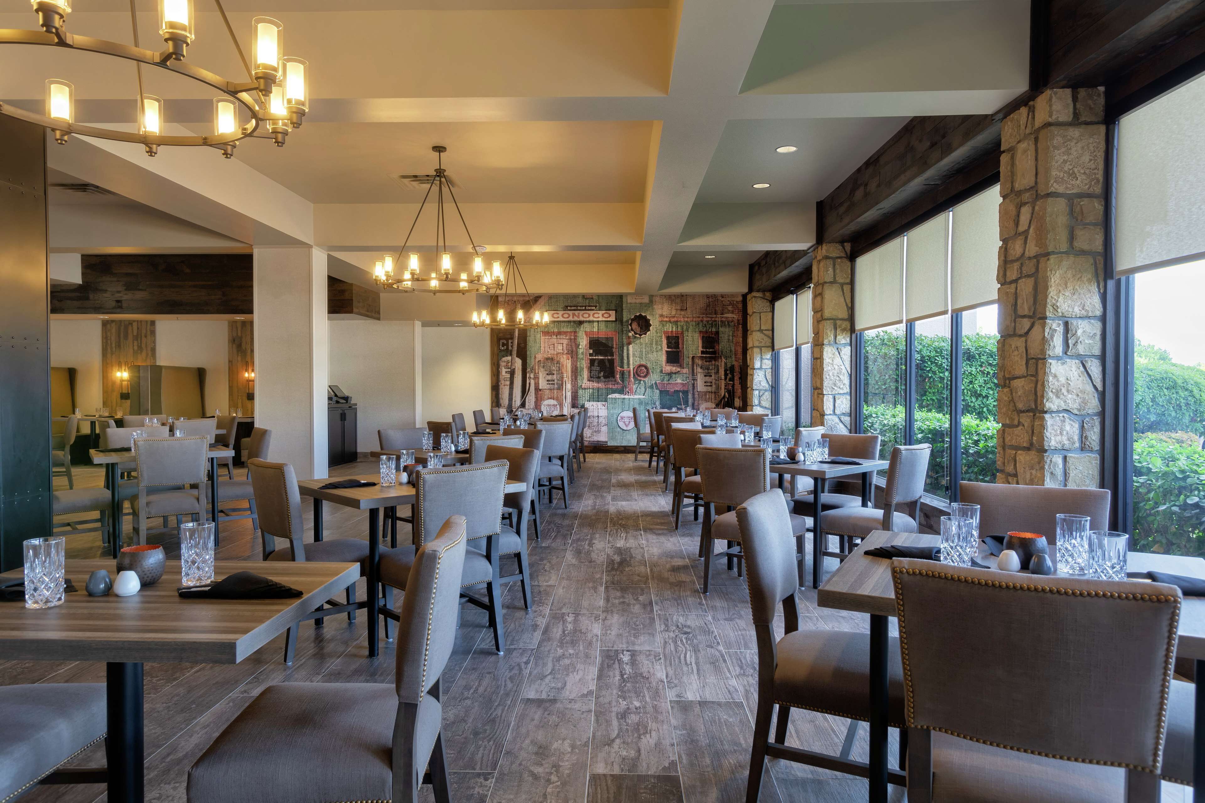 A spacious restaurant with multiple tables and chairs, large windows, and a chandelier.