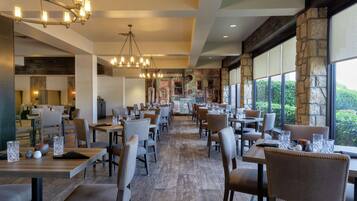 A spacious restaurant with multiple tables and chairs, large windows, and a chandelier.