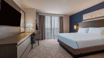 A hotel room with a bed, a desk, a chair, a TV, and a window with curtains.