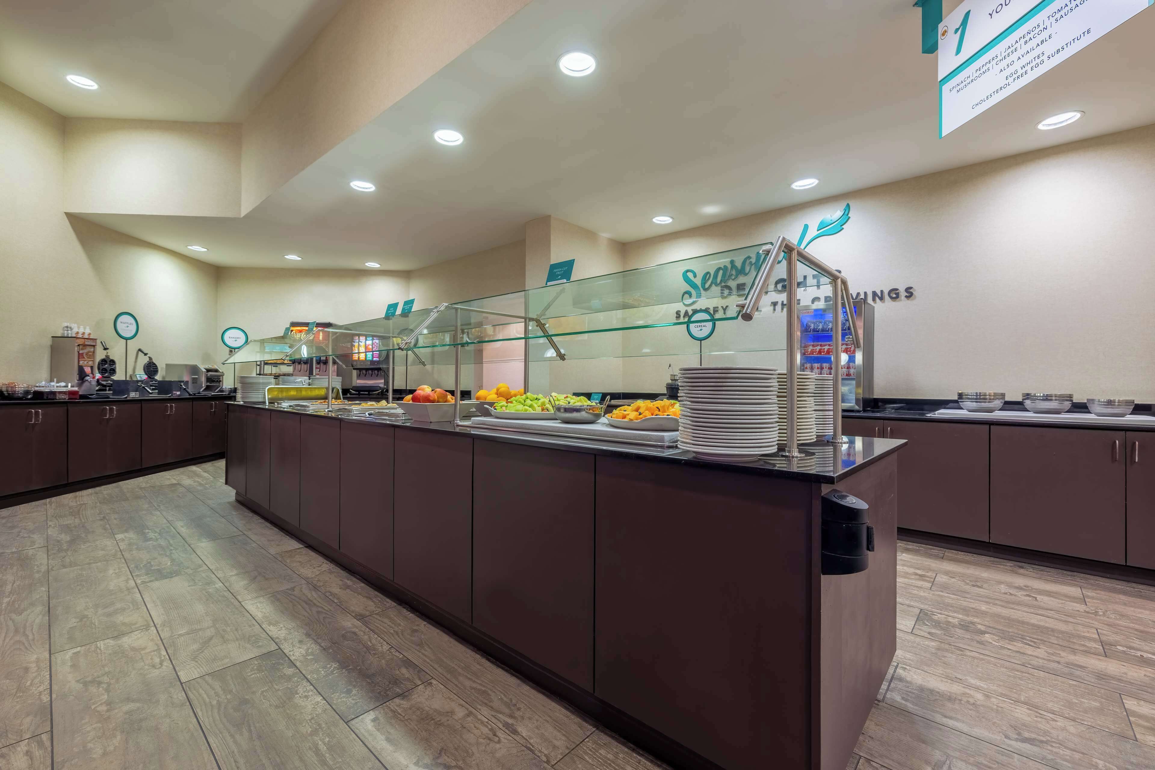 Zona de buffet con mampara de vidrio, diferentes opciones de comida y un cartel que indica 'Ahorros de Temporada'.