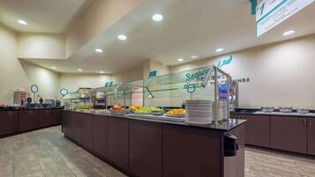 Zona de buffet con mampara de vidrio, diferentes opciones de comida y un cartel que indica 'Ahorros de Temporada'.