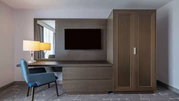 A hotel room with a desk, chair, TV, wardrobe, and a lamp.