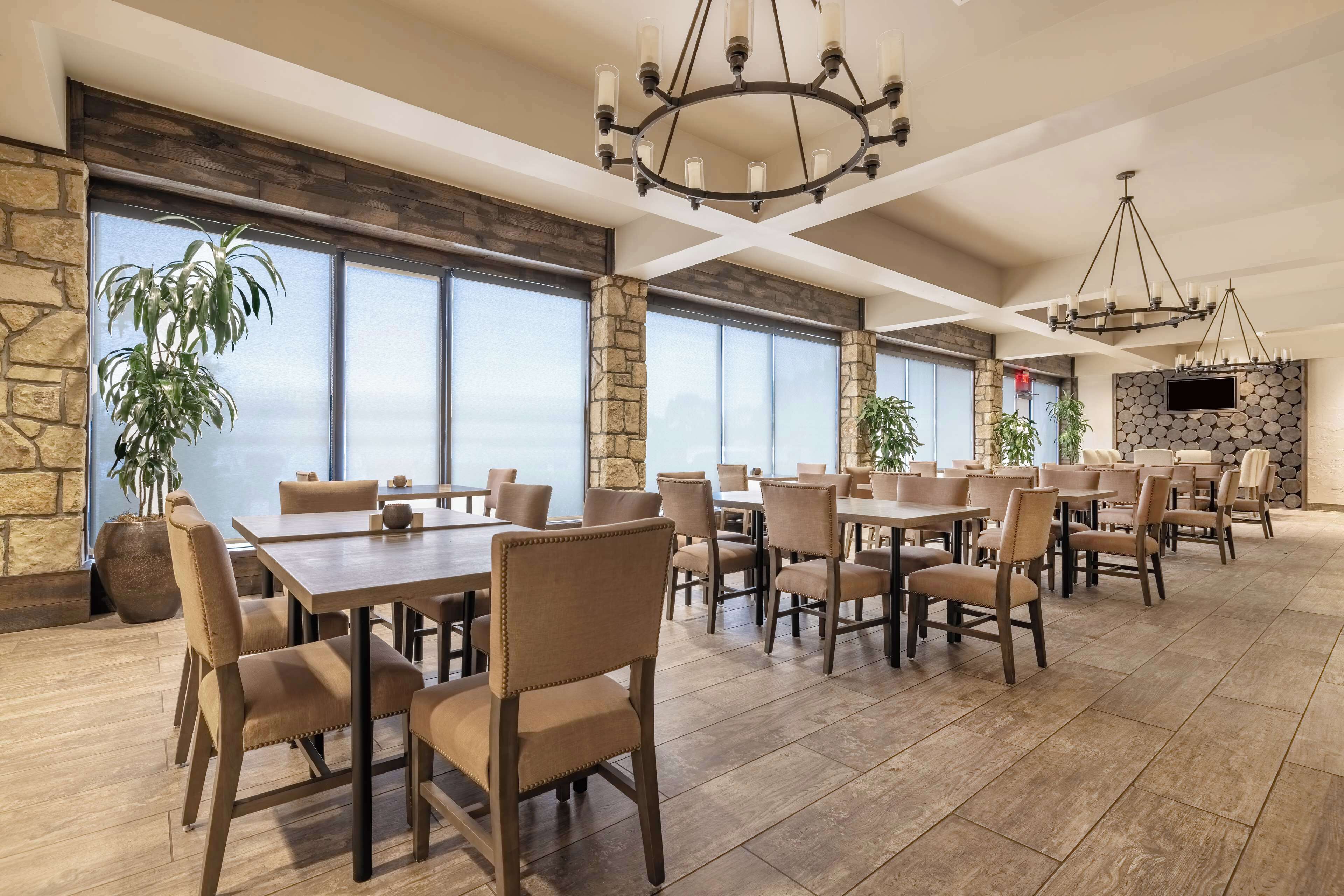 A spacious dining area with multiple tables and chairs, large windows, and a stone accent wall.