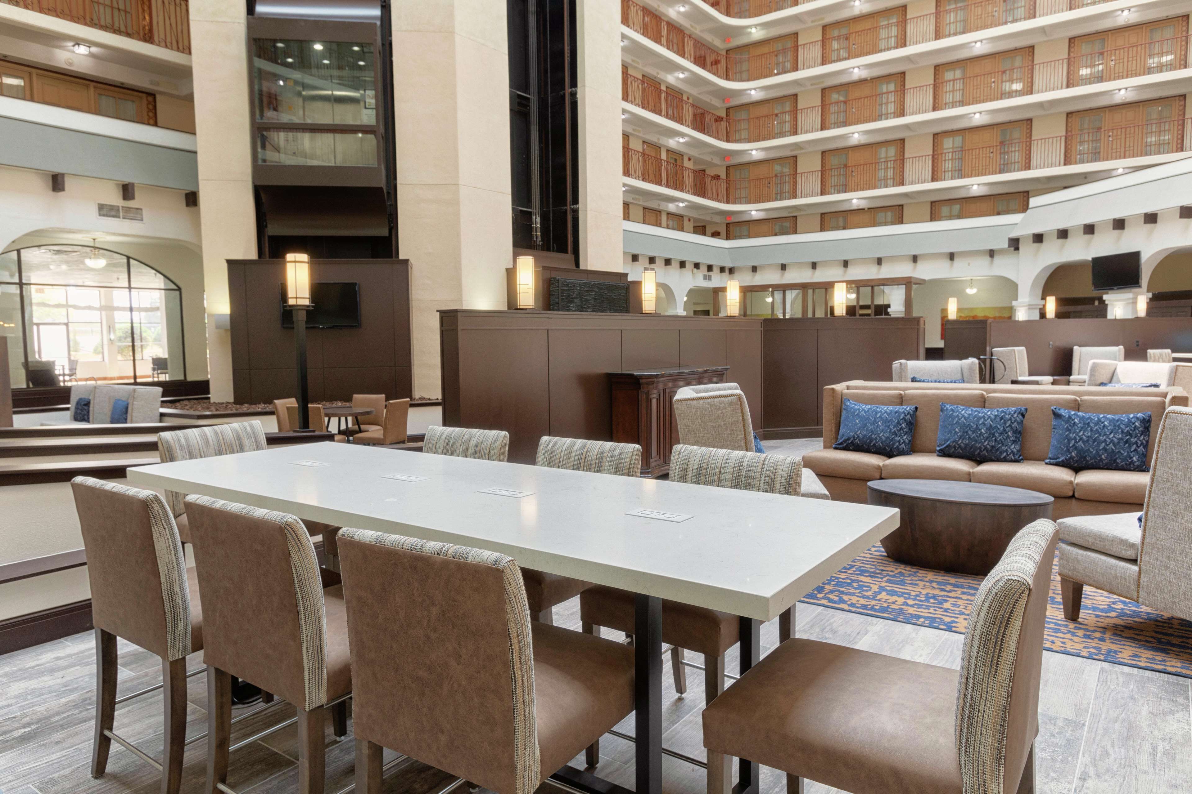 Un hall d’entrée spacieux avec un plafond haut, un espace de détente central agrémenté de canapés et de fauteuils, ainsi qu’une grande table pour les réunions.