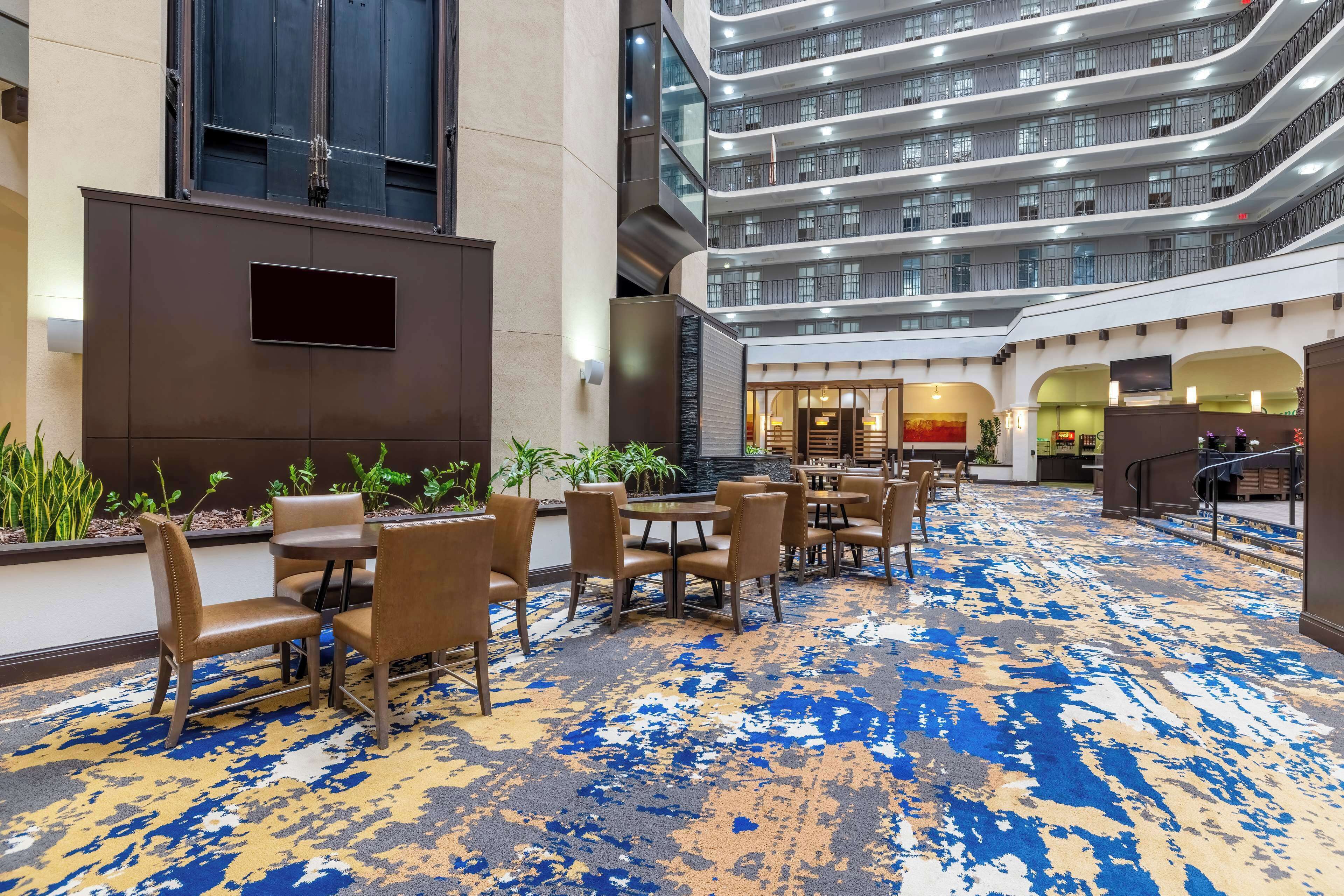 Un vestíbulo de hotel con diseño moderno, que cuenta con un amplio espacio de estar con mesas y sillas, una alfombra estampada y vistas a los pisos superiores.