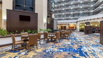 Un vestíbulo de hotel con diseño moderno, que cuenta con un amplio espacio de estar con mesas y sillas, una alfombra estampada y vistas a los pisos superiores.