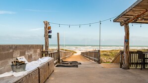 Un paseo marítimo en la playa con una terraza de madera, luces colgantes y vistas al océano.
