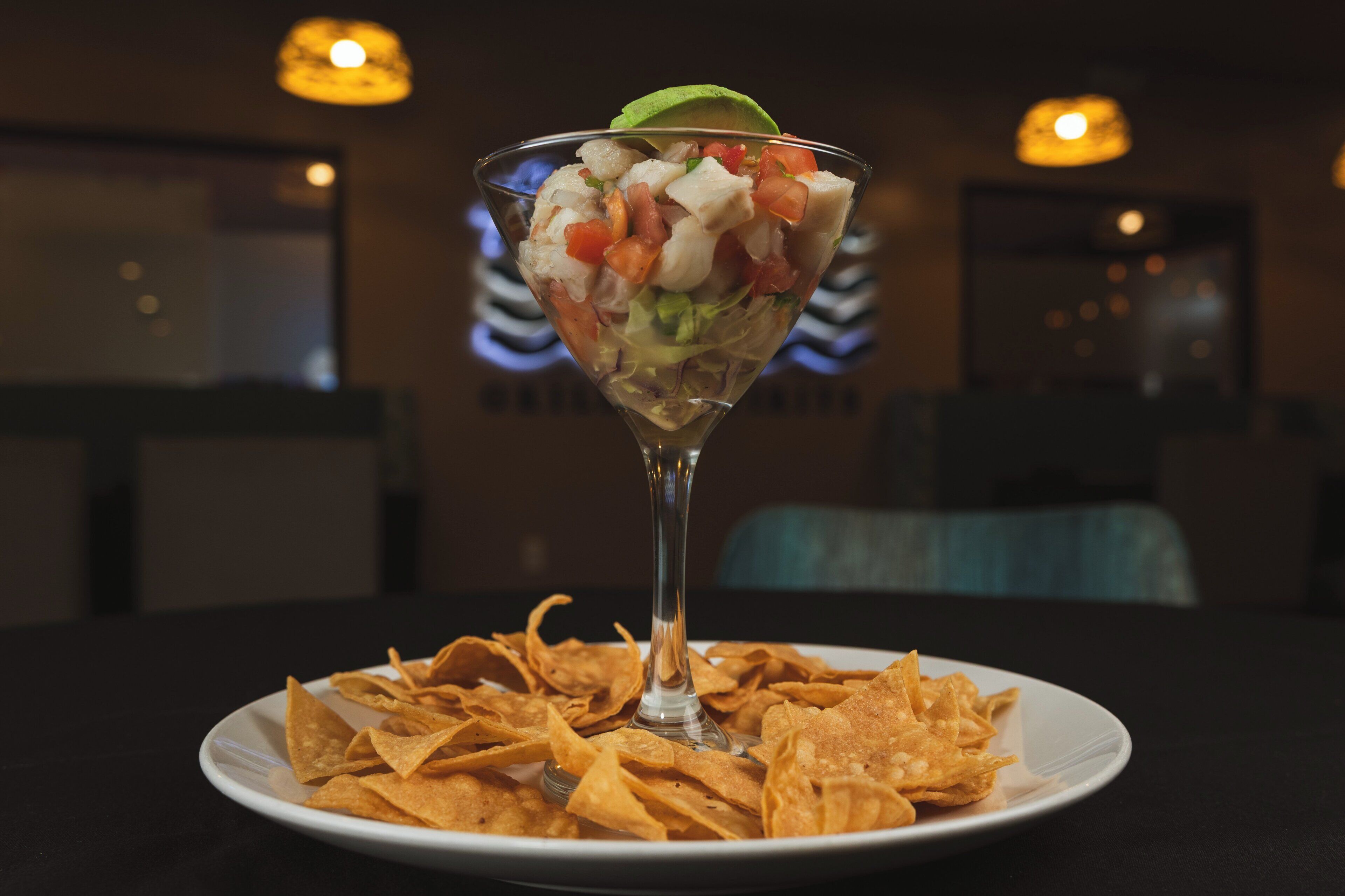 Un cocktail servi dans un verre, accompagné d’une assiette de chips de tortillas.