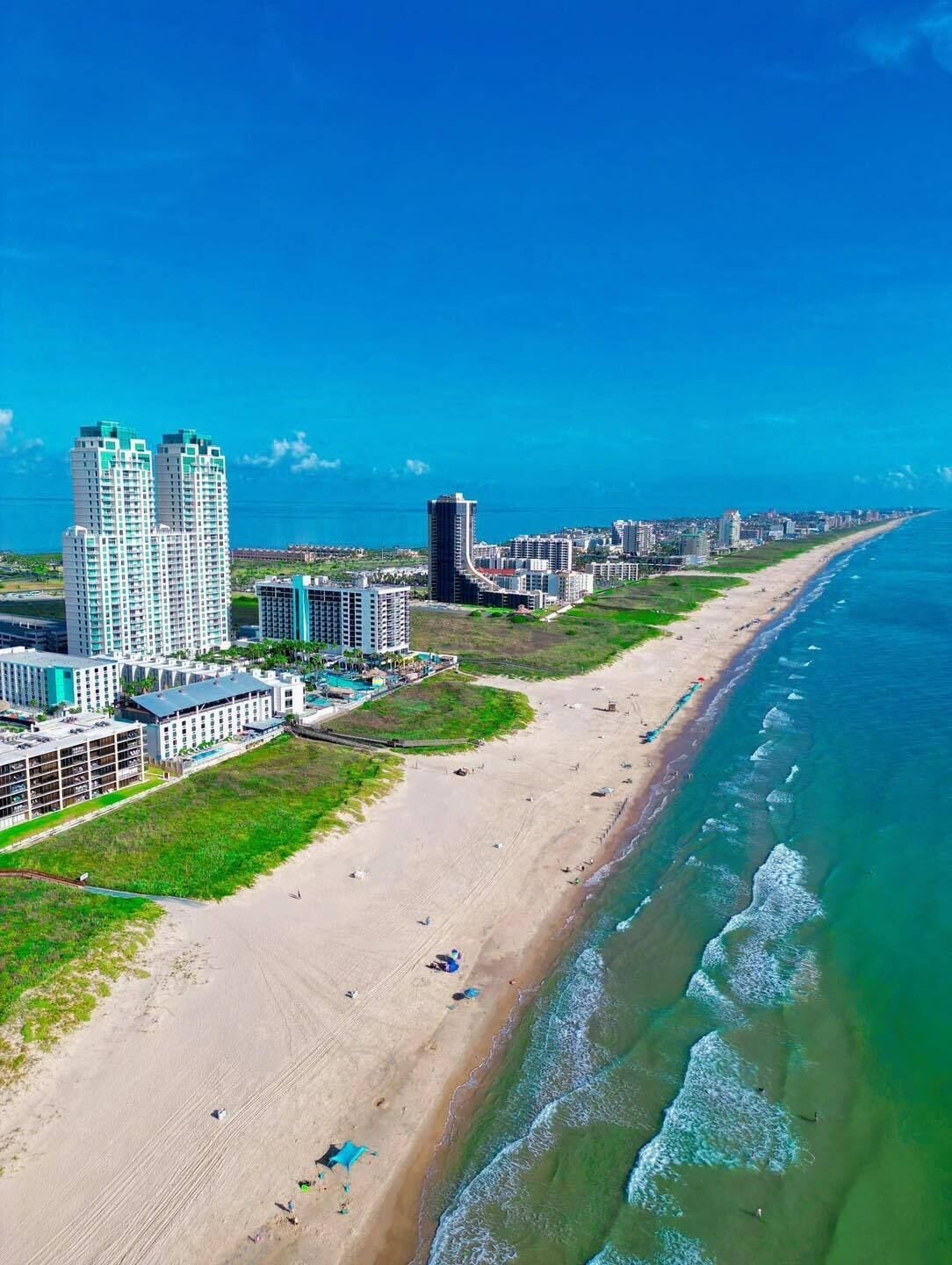 An aerial view of a coastal city with high-rise buildings, a wide sandy beach, and the ocean.