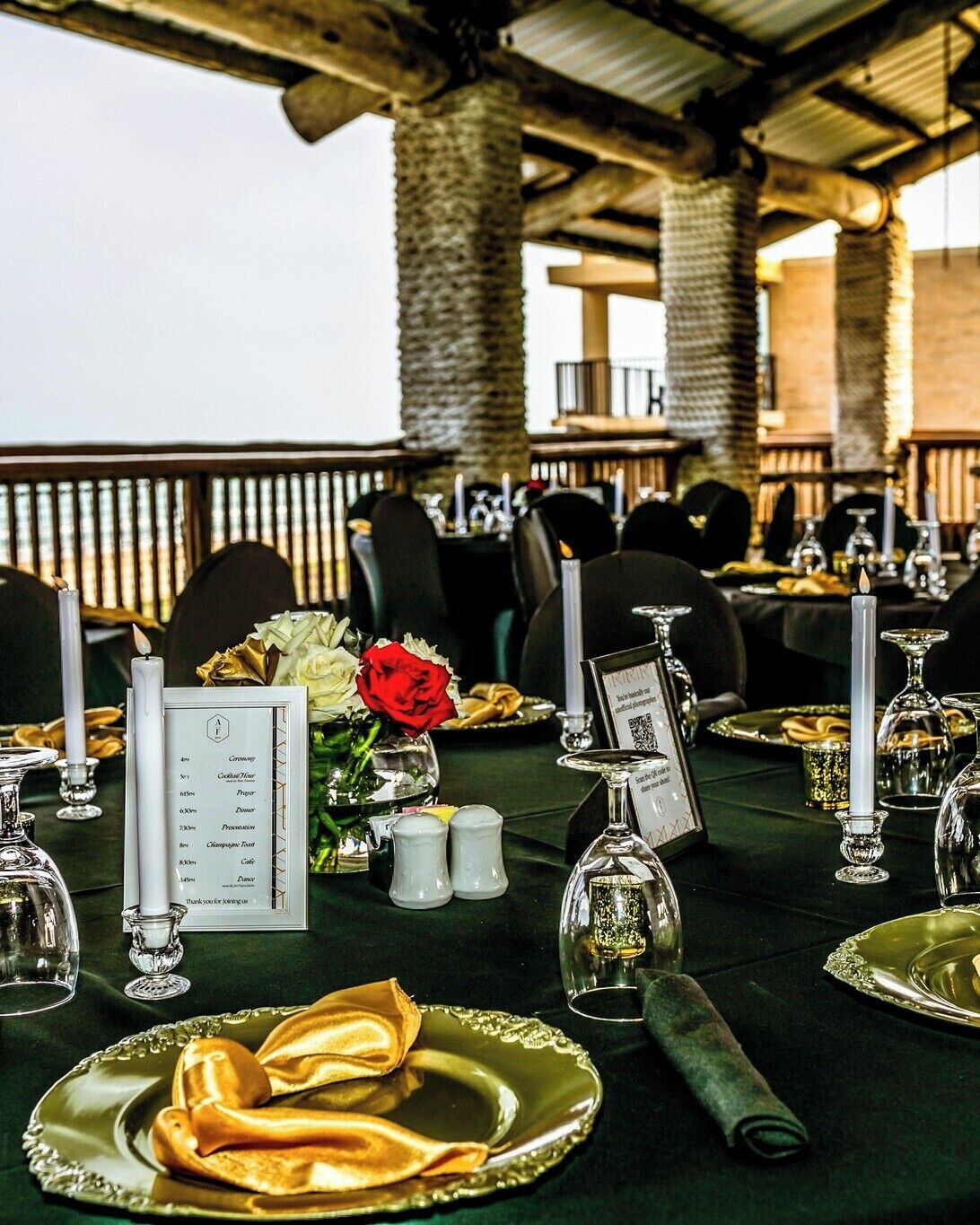 A formal outdoor dining setup with tables set for a meal, featuring elegant tableware and candle holders.