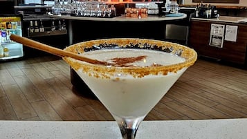 A martini glass with a salted rim on a bar counter. In the background, there is a bar area with various bottles and glasses.