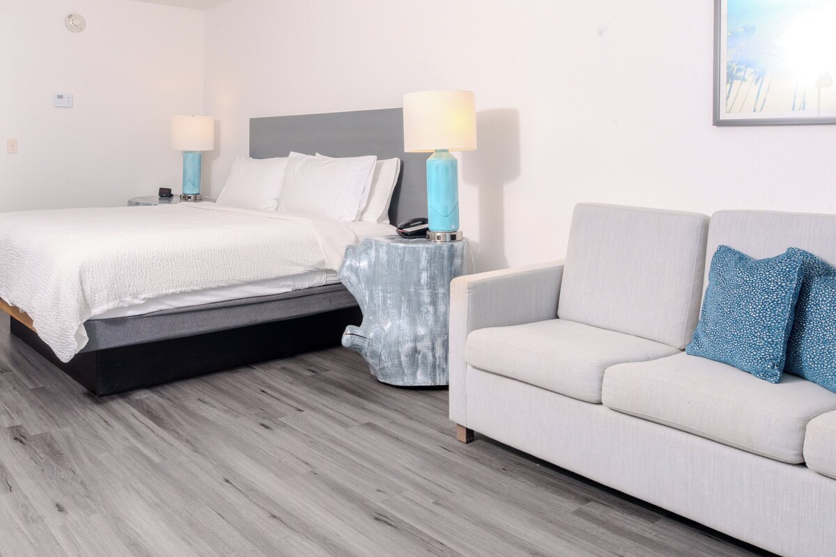 A hotel room with a bed, a sofa, and a nightstand with lamps.