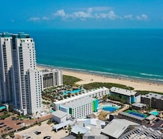 A high-rise hotel with a beach view, multiple swimming pools, and a tennis court.