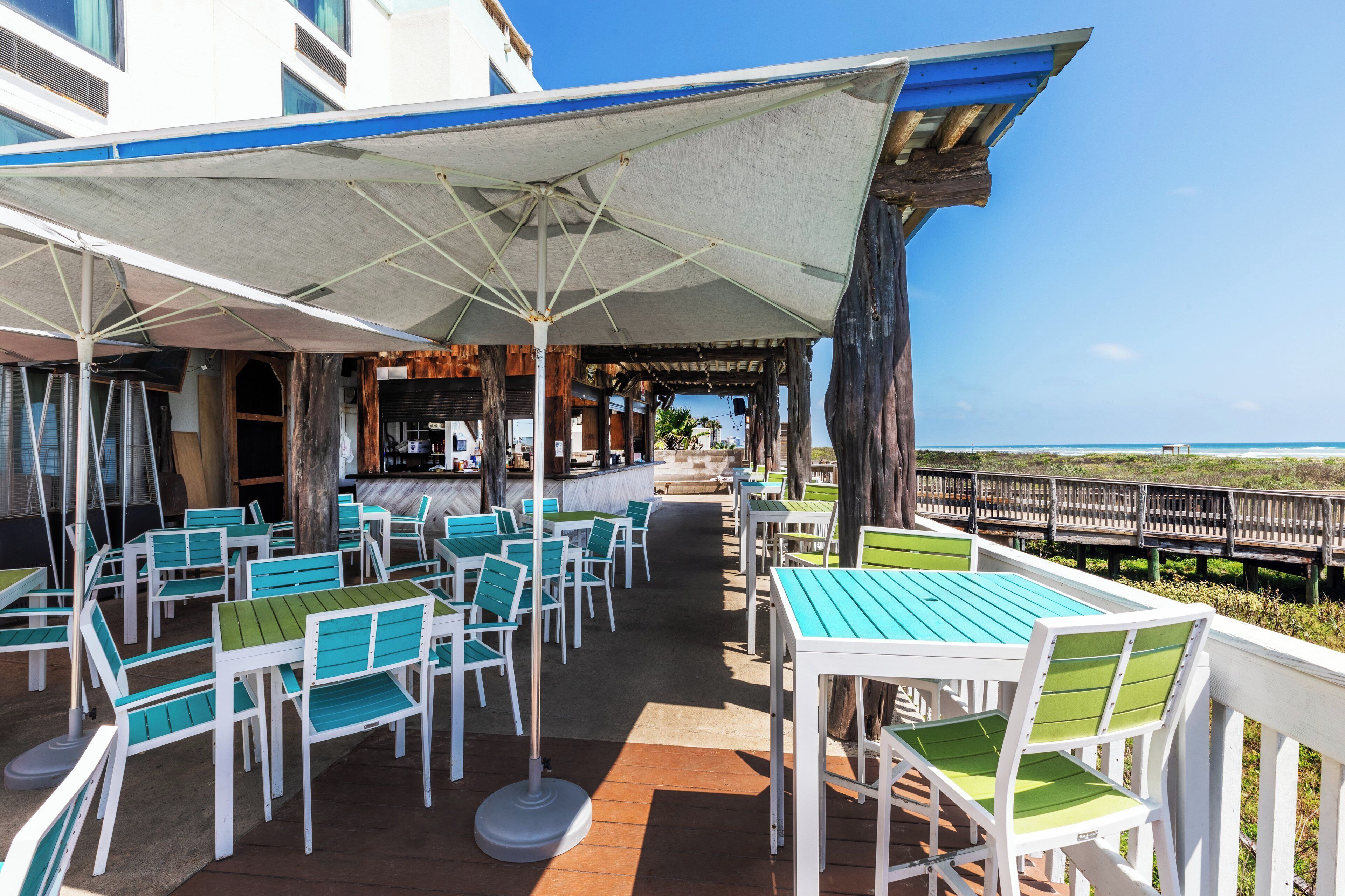 Ein Sitzbereich im Freien mit Tischen, Stühlen und einer Bar, mit Blick auf das Meer.