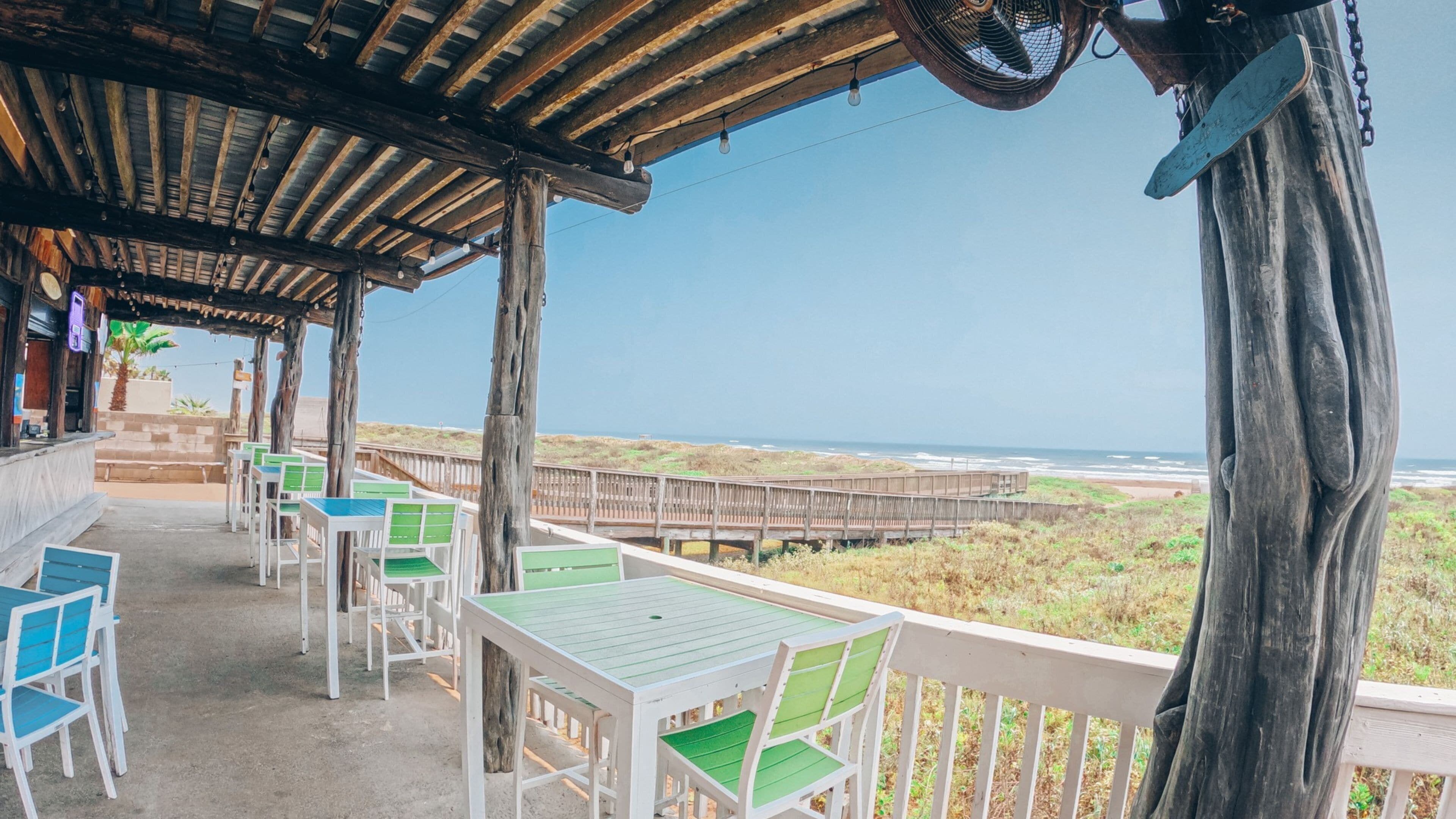 A beachside terrace with wooden tables and chairs, overlooking the ocean.