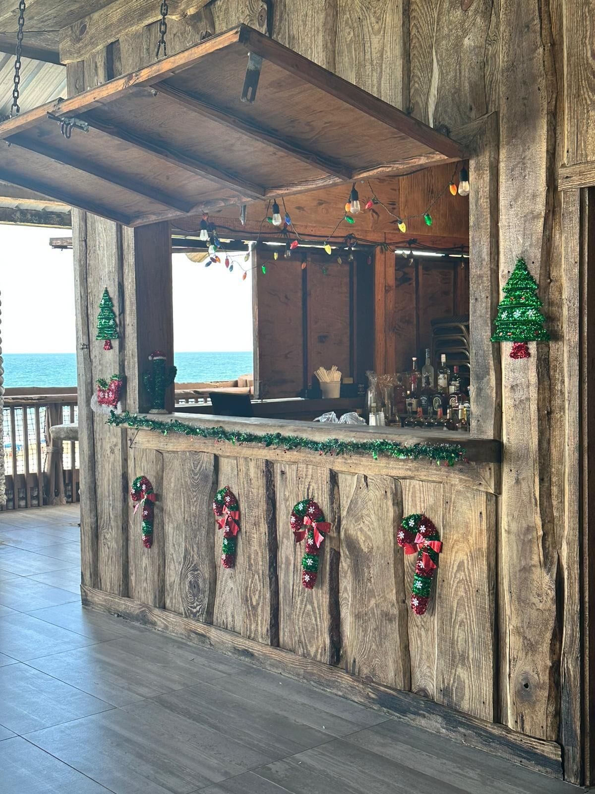 Una zona de bar rústica de madera con vista al océano, decorada con adornos navideños.