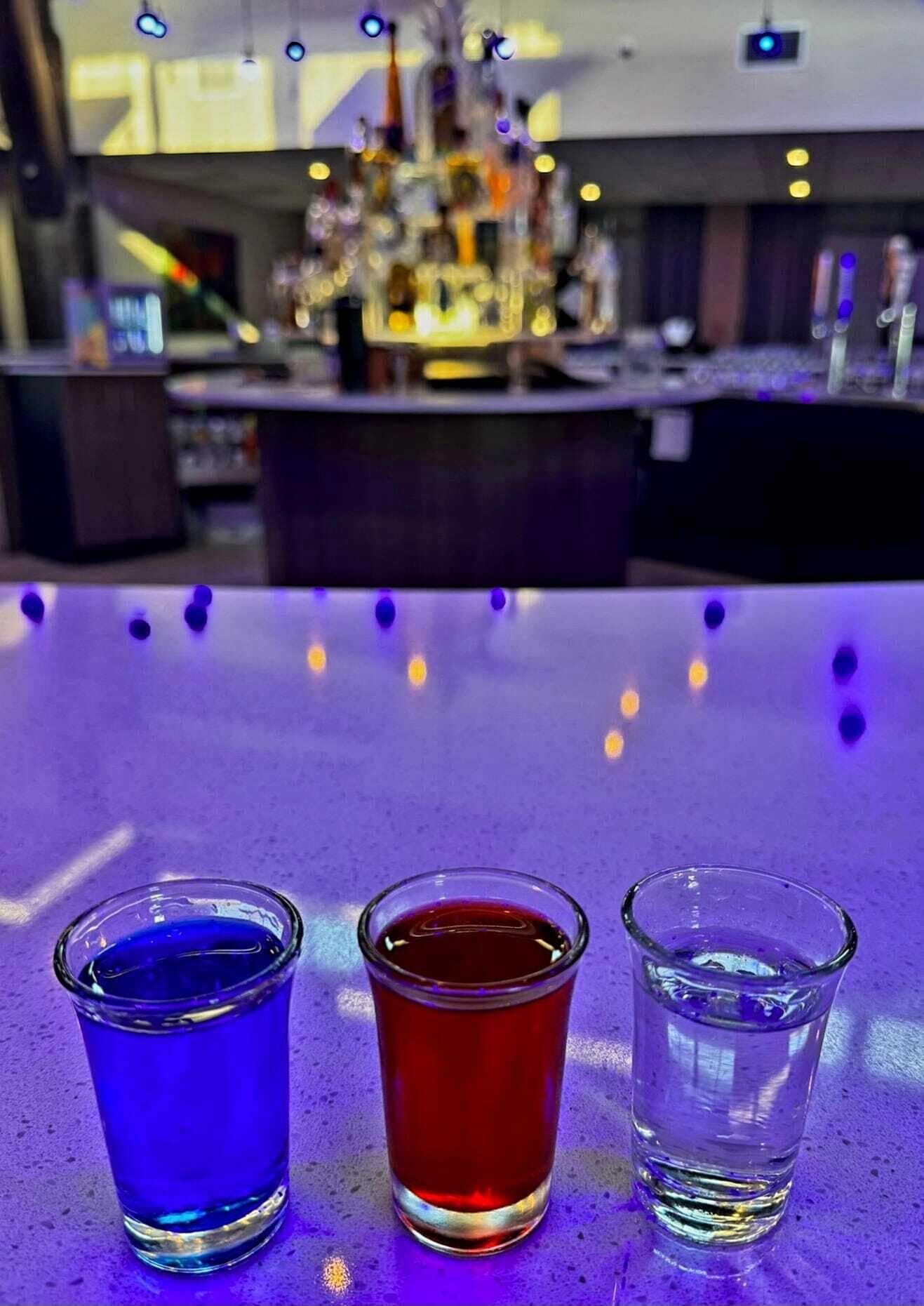 Tre bicchierini su un tavolo con un bar sullo sfondo.