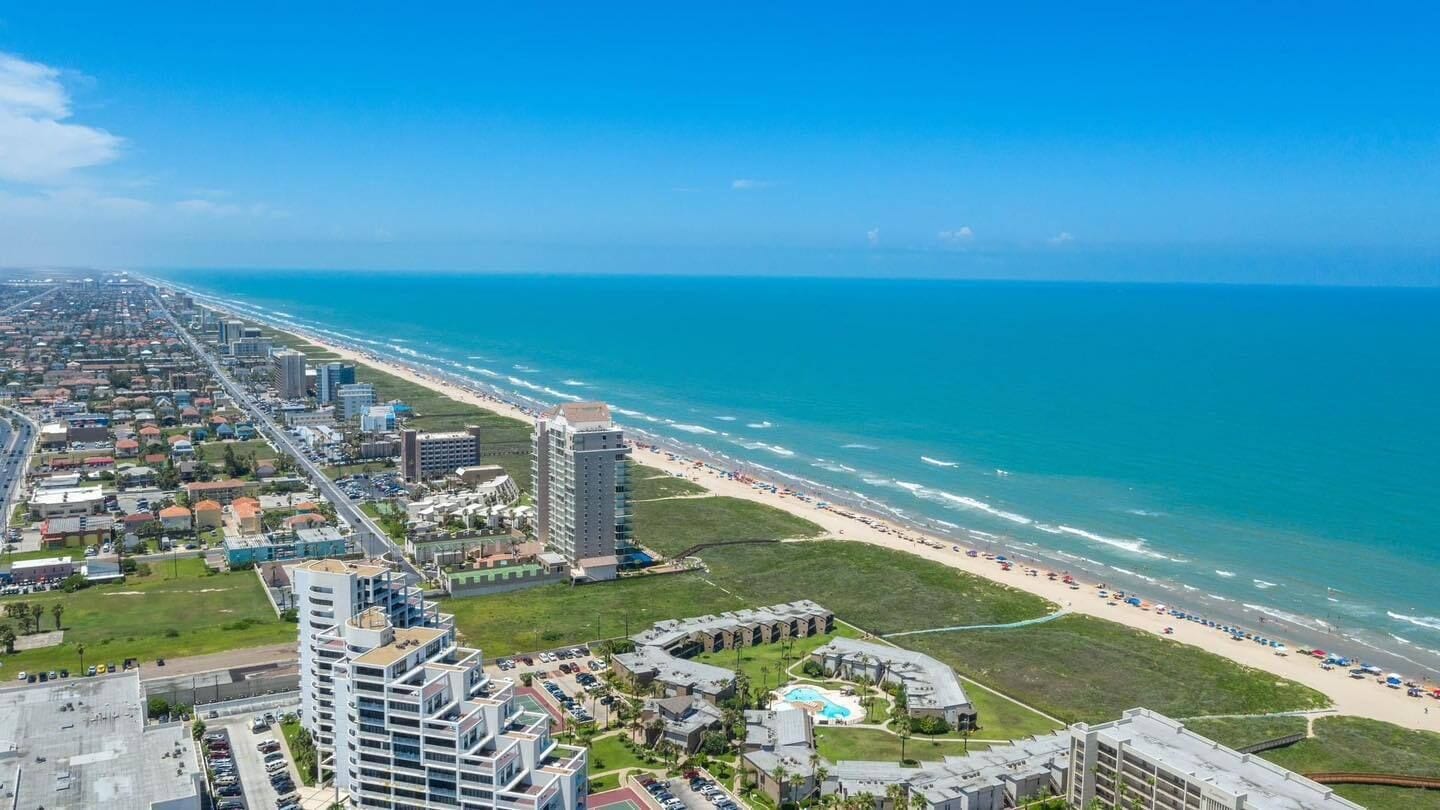 Vue aérienne d’une ville côtière avec une plage, des immeubles de grande hauteur et un parking.