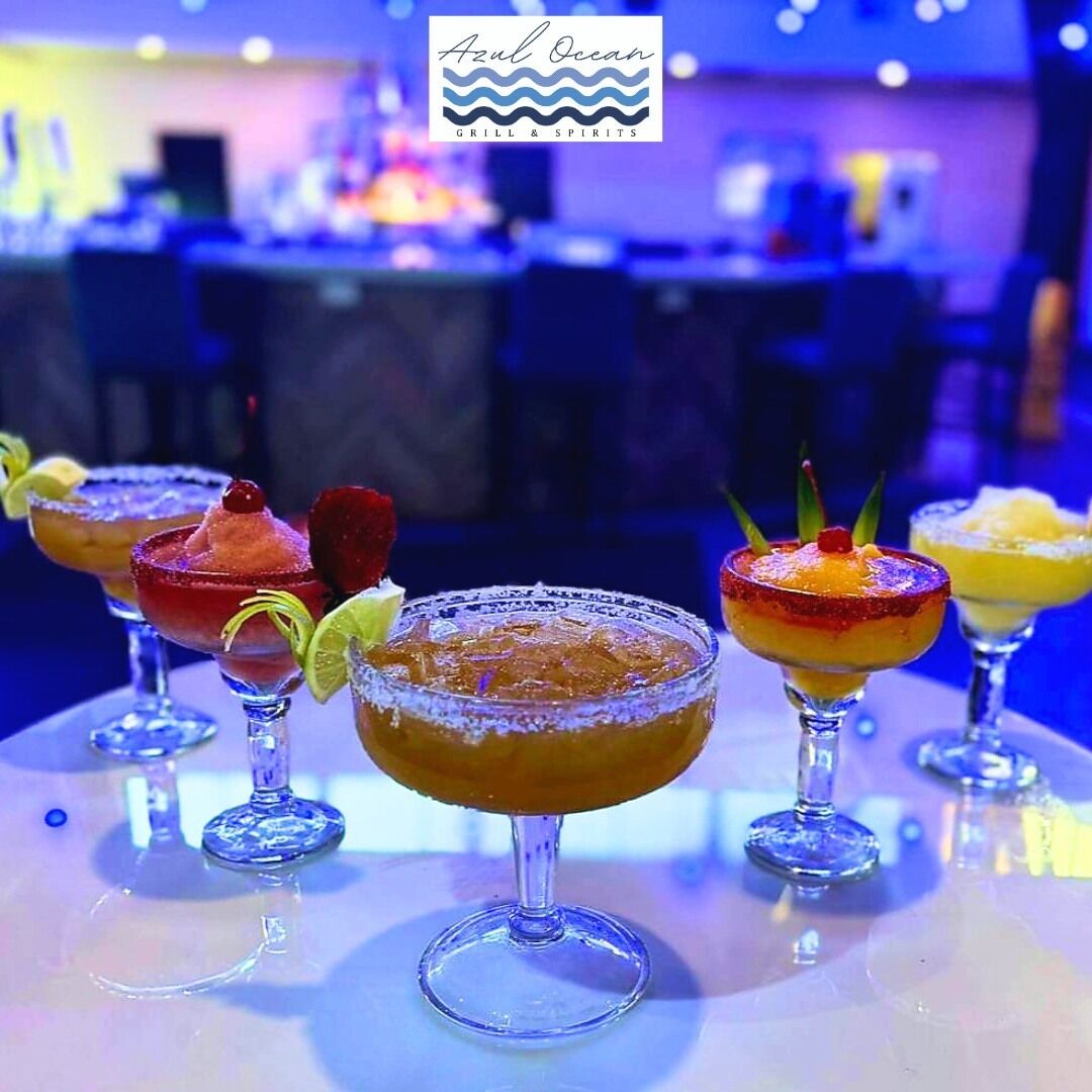 A bar area with a variety of colorful cocktails in martini glasses, a logo for 'Azure Ocean Grill & Spirits' above the bar, and a blurred background suggesting a busy venue.
