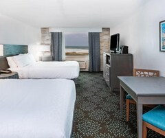 A hotel room with two beds, a desk, a chair, a TV, and a view of the beach.