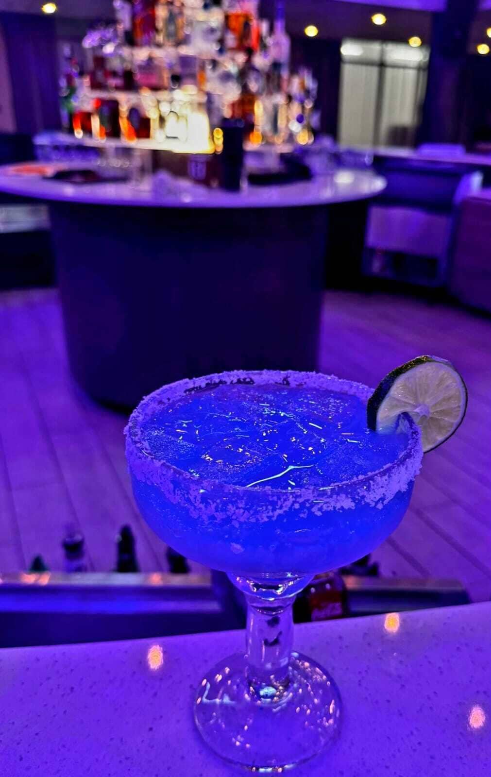 A blue margarita with a lime garnish on a bar counter.