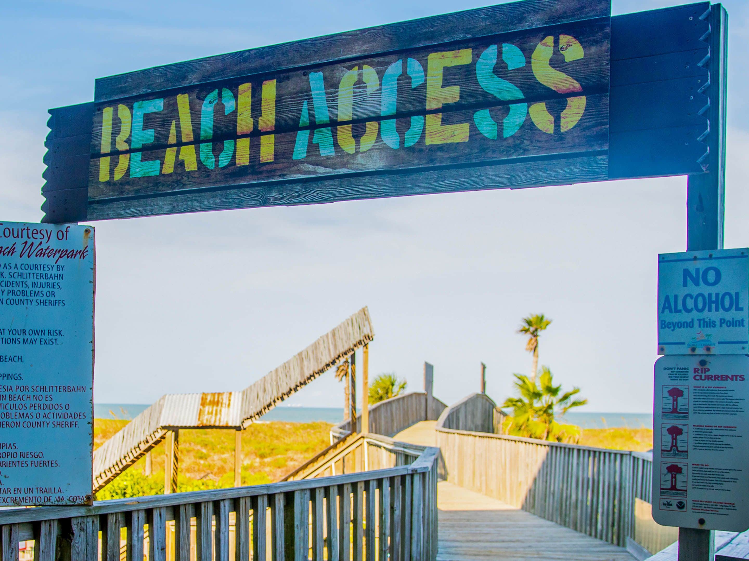 A wooden boardwalk leading to a beach with a 'Beach Access' sign overhead.