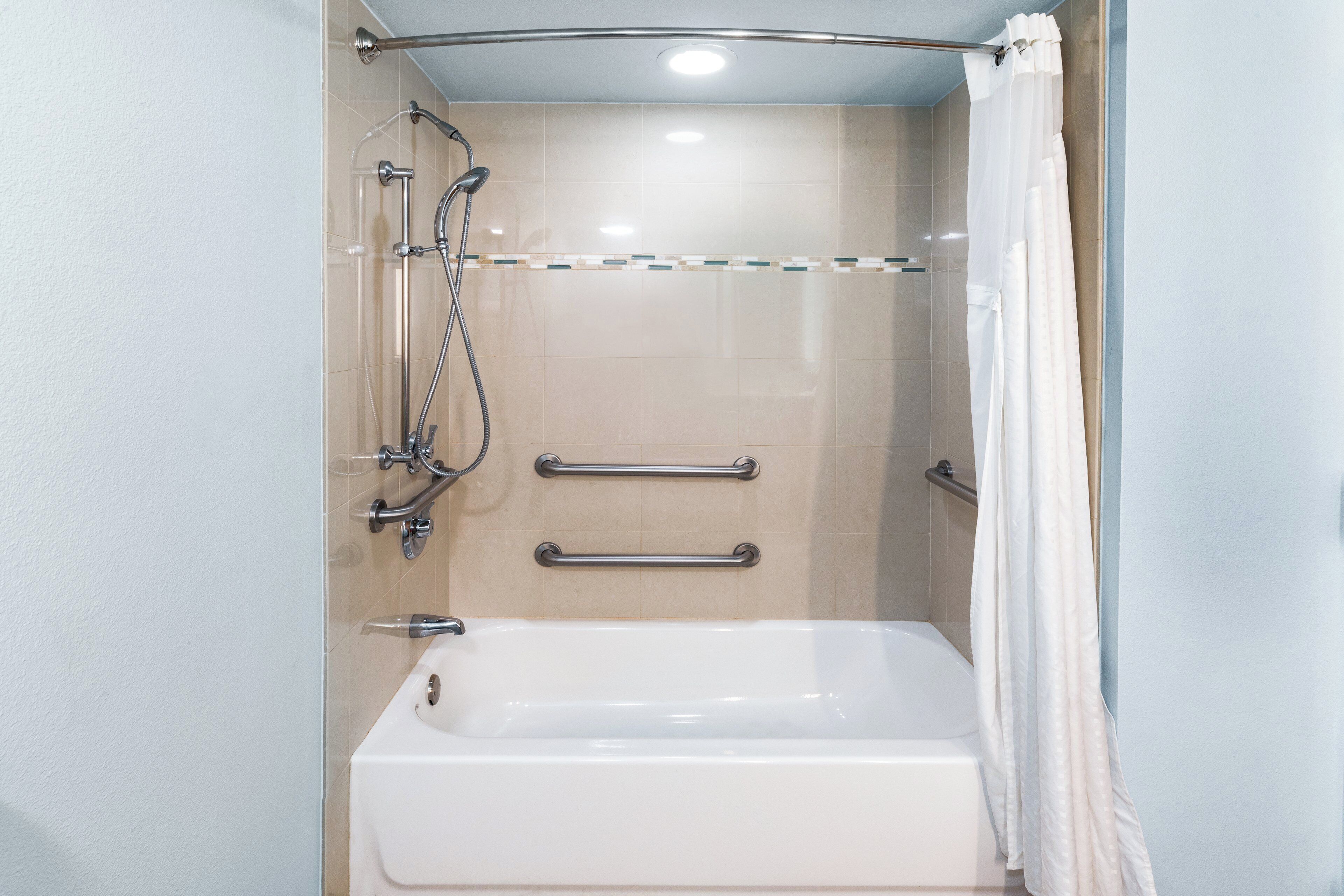 A modern bathroom with a bathtub, shower, and grab bars.