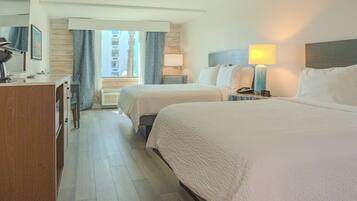 A hotel room with two beds, a desk with a lamp, and a view of the city through the window.