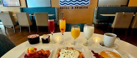 Un desayuno con platos de comida, bebidas y un letrero de neón que dice 'Azul Caribbean GRILL & SPIRITS'.
