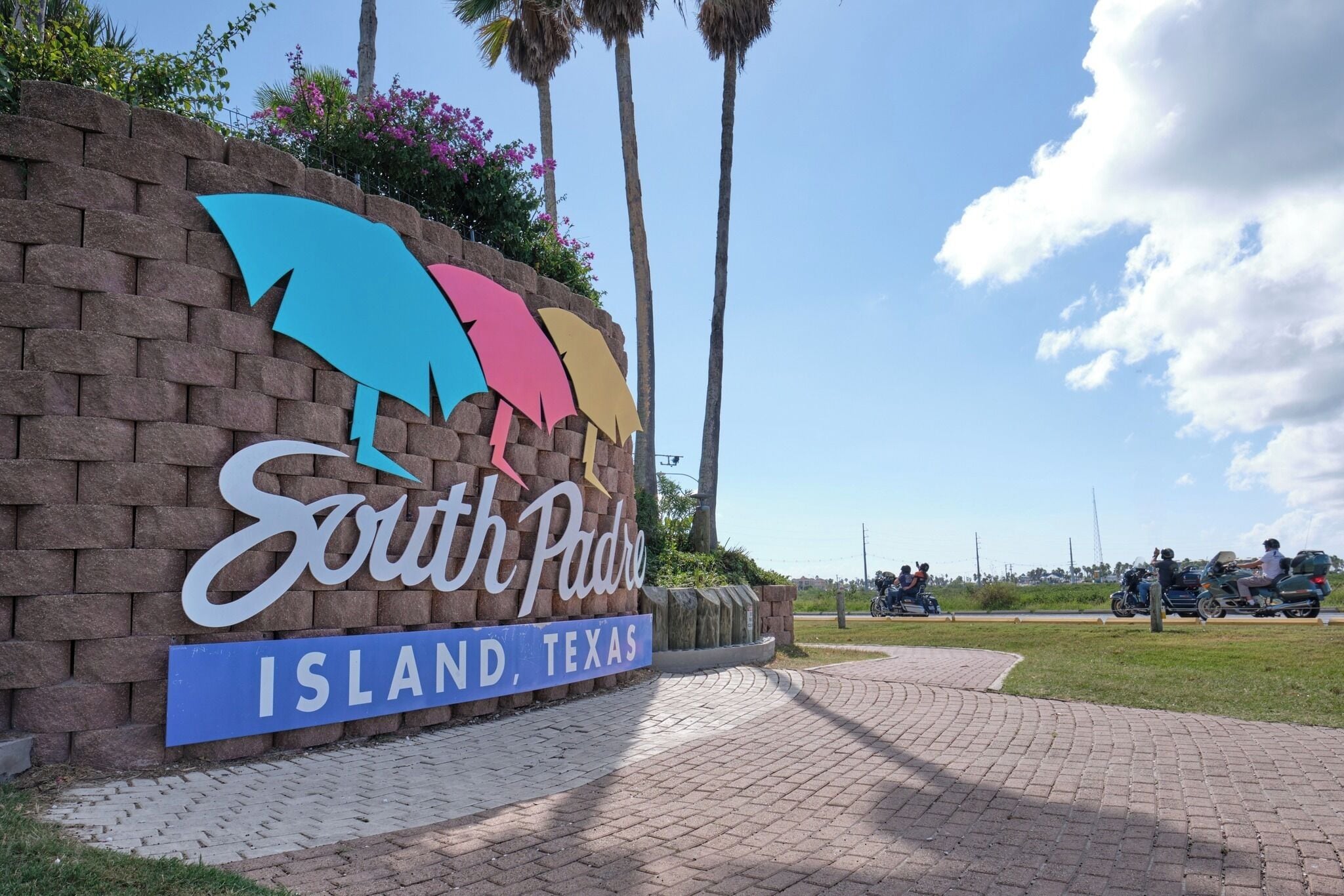 A sign for South Padre Island, Texas, with palm trees and a clear sky in the background.