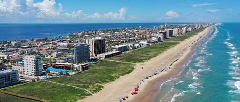 A coastal cityscape with a long sandy beach lined with buildings and a clear blue sky.